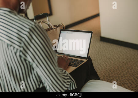 Woman sitting on bed in hotel room working on laptop computer. Female executive using laptop. Working form hotel room. Stock Photo