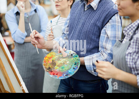 Mid section portrait of unrecognizable artist holding palette while working with group of students in art class, copy space Stock Photo
