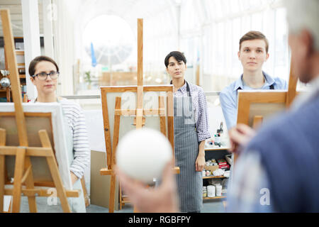 Portrait of group of art students standing in row at easels and listening to teacher during lecture in class Stock Photo