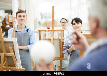 Portrait of group of cheerful art students standing in row at easels and listening to teacher during lecture in class Stock Photo