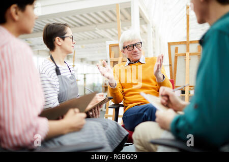 Portrait of mature art teacher talking to group of students sitting in circle in art studio Stock Photo