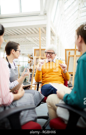 Portrait of joyful mature art teacher talking to group of students sitting in circle in art studio Stock Photo
