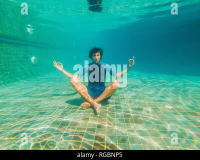 young man in black bikini in yoga position underwater in diving aquarium, full body shot, front view Stock Photo