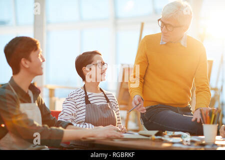 Portrait of mature art teacher working with group of students in sunlit art studio, copy space Stock Photo