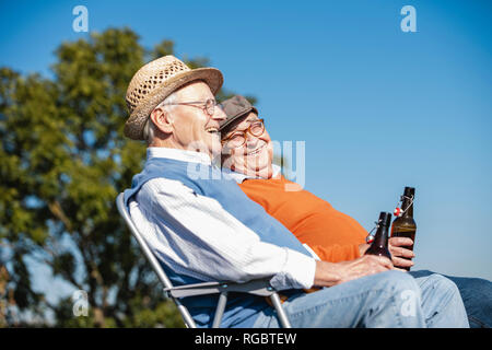 Two old friends sitting in the fields, drinking beer, talking about old times Stock Photo