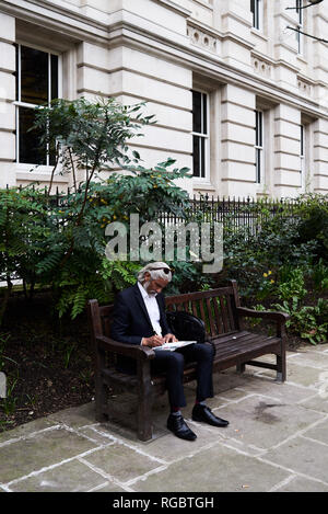 Senior businessman sitting on bench outdoors writing notes in notebook Stock Photo