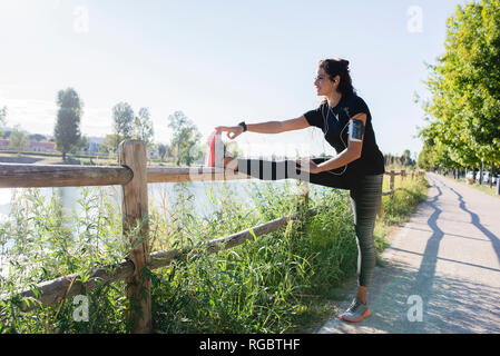 Sportive young woman stretching her leg at the riverside Stock Photo