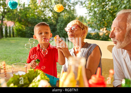 Grandmother and grandson blowing soap bubbles on a garden party Stock Photo
