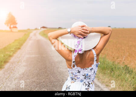 Rear view of mature woman wearing hat on remote country lane in summer Stock Photo