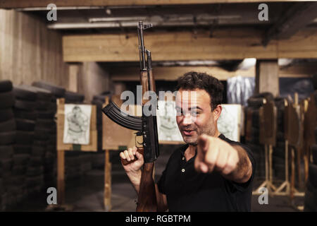 Portrait of man with a rifle pointing his finger in an indoor shooting range Stock Photo