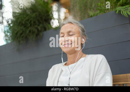 Smiling senior woman with closed eyes wearing earphones outdoors Stock Photo