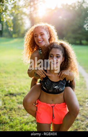 Portrait of happy young woman giving her laughing twin sister a piggyback ride Stock Photo