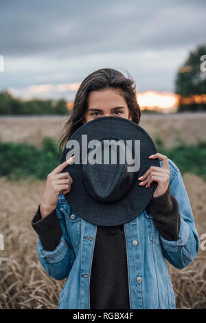 Portrait of young woman hiding behind black hat Stock Photo