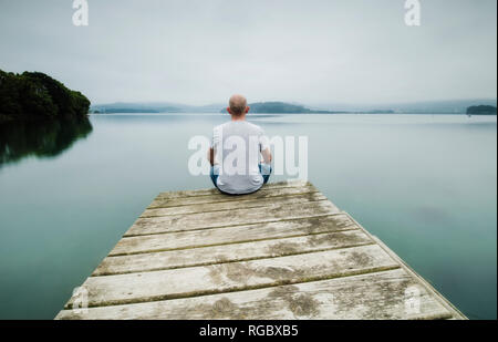 Back view of man sitting on jetty looking at distance Stock Photo