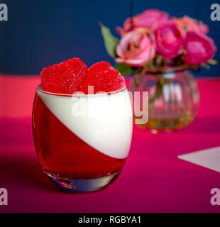Italian dessert Panna Cotta with candy in shape of hearts on pink and blue background in Valentines Day Stock Photo