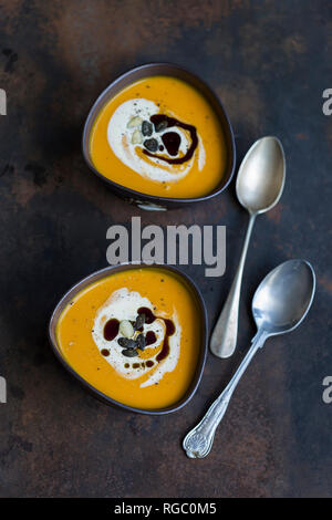 Two bowls of homemade Hokkaido pumpkin soup garnished with cream, pumpkin seed oil and pumpkin seed Stock Photo