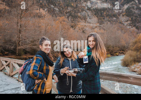 Spain, portrait of three young women with instant photos on a bridge in Ordesa National Park Stock Photo