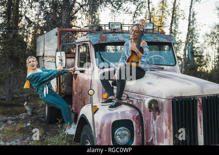 Two friends sitting on a broken truck, playing the ukulele Stock Photo
