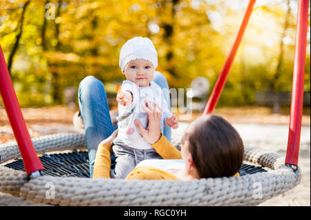 Portrait of baby girl relaxing with her mother on a swing in autumn Stock Photo