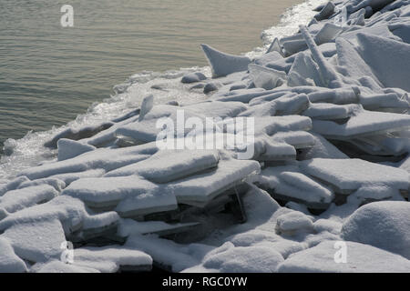 Long line of rocks along Lake Michigan shoreline covered with frozen ice and snow on a sunny winter day. Stock Photo