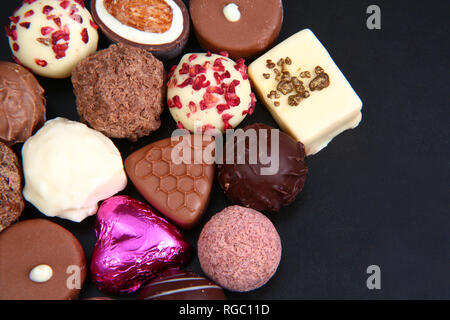 Close up of a selection of luxary chocolates, with a foil wrapped pink heart, which could be for Valentines Day. Stock Photo