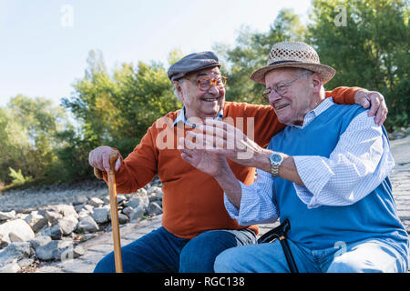 Two old friends sitting by the riverside, having fun Stock Photo