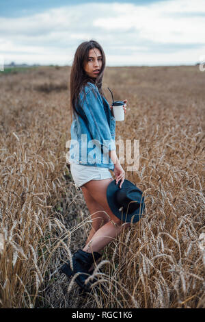 Portrait of young woman with beverage walking in corn field Stock Photo