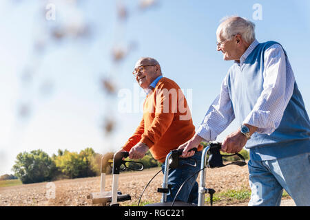 Two old friends walking on a country road, using wheeled walkers Stock Photo