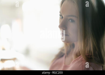 Portrait of daydreaming young woman behind glass pane Stock Photo