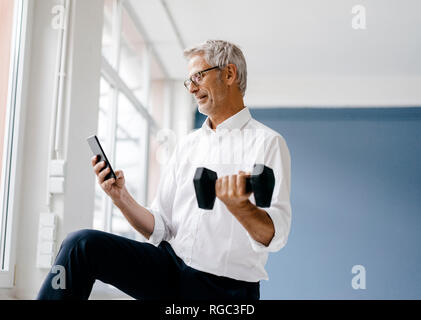 Successful manager using smartphone and training with a dumbbell Stock Photo