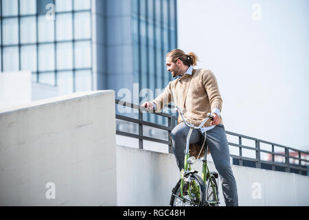 Young man sitting on bicycle, waiting at a railing Stock Photo