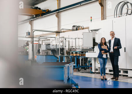 Businessman an woman in high tech enterprise, having a meeting in factory workshop Stock Photo