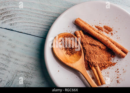 Cinnamon sticks and ground spice on white plate over light wooden background. View from above. Stock Photo