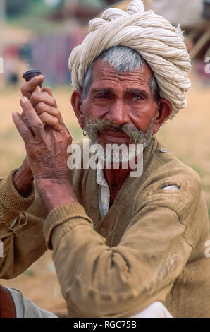 Portrait of an old indian man staring sideways while holding a chillum, white turban and traditional clothes. Shot at the Pushkar Camel Fair, India Stock Photo