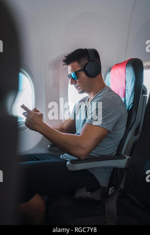Man in airplane, using smartphone, headphones Stock Photo