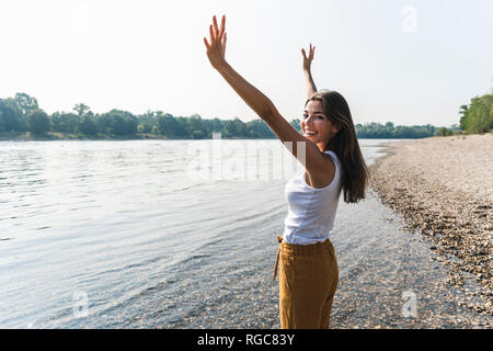 Happy young woman standing at the riverside raising her arms Stock Photo