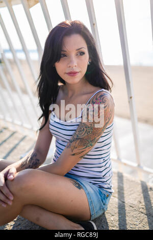 Portrait of young woman with nose piercing and tattoos sitting on balcony at backlight