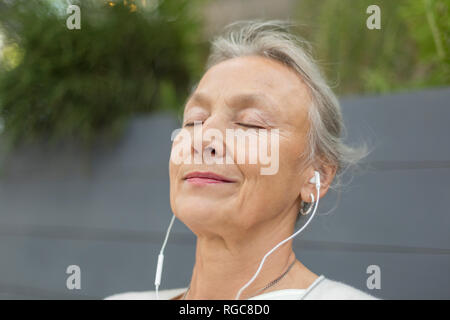 Portrait of senior woman with closed eyes wearing earphones outdoors Stock Photo