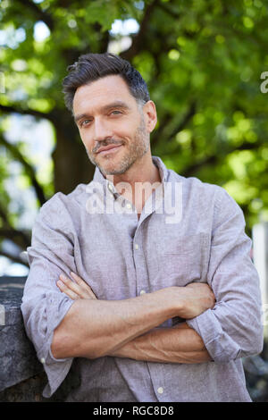 Portrait of smiling mature man with arms crossed leaning against wall Stock Photo