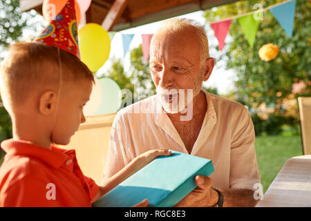 Grandfather handing over present to grandson on a garden birthday party Stock Photo