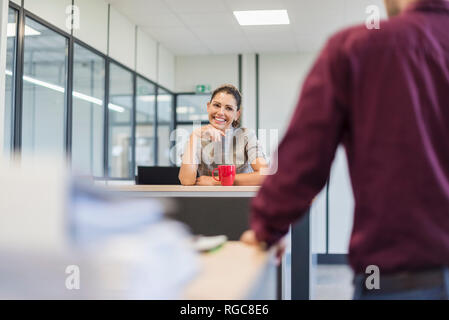 Female employee sitting at desk, talking to colleague Stock Photo