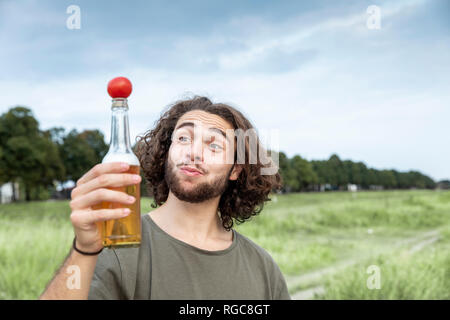 Portrait of smiling young man outdoors balancing tomato on beer bottle Stock Photo