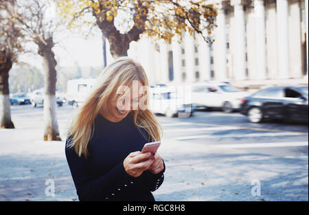Smiling blond woman using smartphone in the city Stock Photo