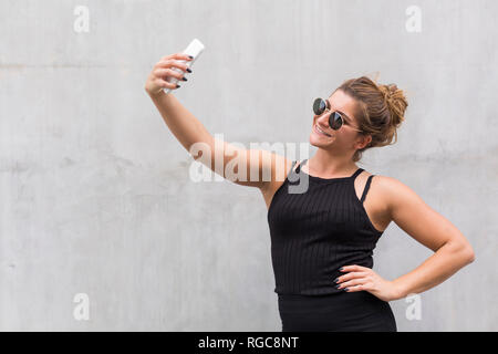 Portrait of smiling young woman dressed in black taking selfie with smartphone