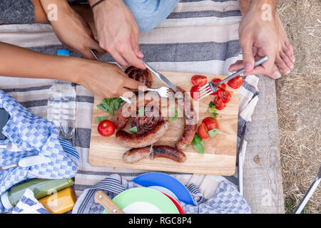 Close-up of couple eating fried sausages and tomatoes outside Stock Photo
