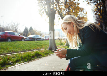 Smiling blond woman using smartphone outdoors Stock Photo