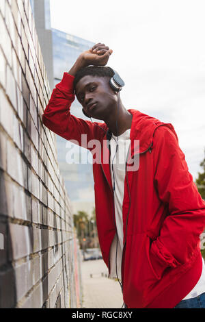 Young black man leaning on wall, listening music with headphones Stock Photo