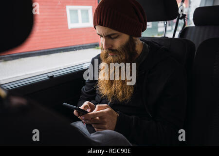 Bearded young man sitting on back seat of a car checking cell phone Stock Photo