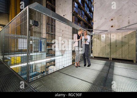 Women using laptop in high rack warehouse Stock Photo