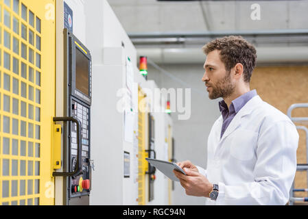 Employee checking manufacturing machines in high tech company, using digital tablet Stock Photo